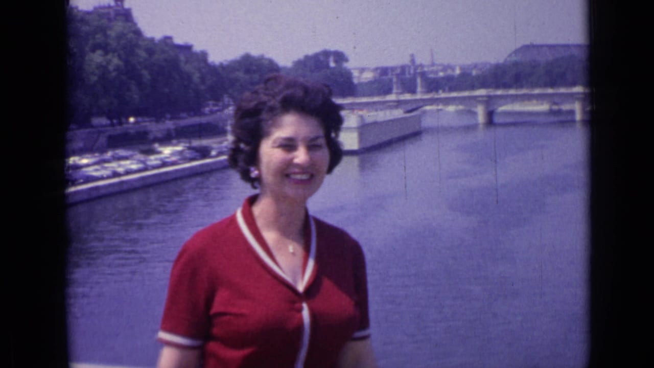 Woman in a red shirt smiles slightly to one side near a river and bridge.