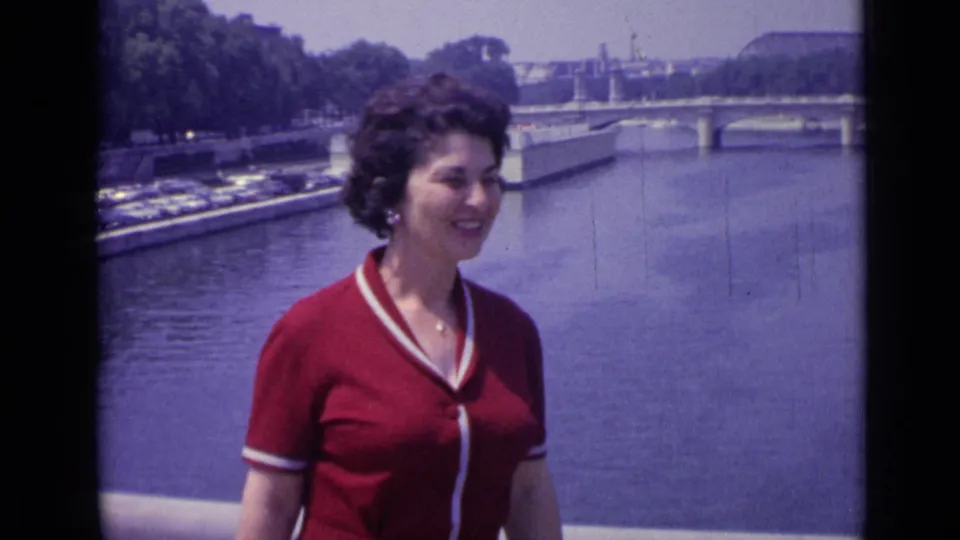 A profile view shows the woman smiling beside the Versailles river, with bridge railings, water, trees, and parked cars in the background.
