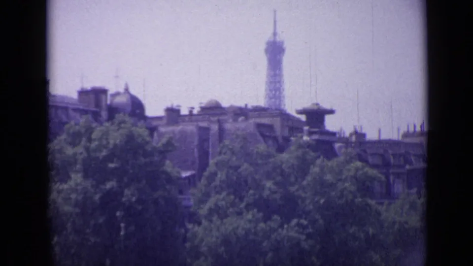 A second distant view shows the Eiffel Tower above Paris rooftops and dense trees, with home-movie softness and slight blur.