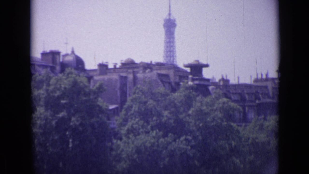 Distant tower and rooftops seen beyond trees with dark film gate edges.