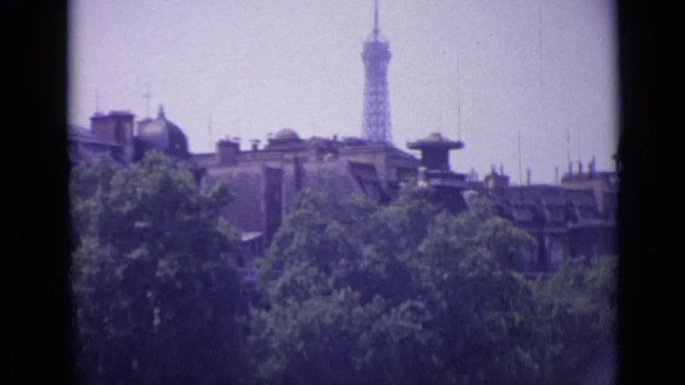 1962 8mm frame from France showing a distant tower-like landmark above rooftops and trees, framed by dark film borders.