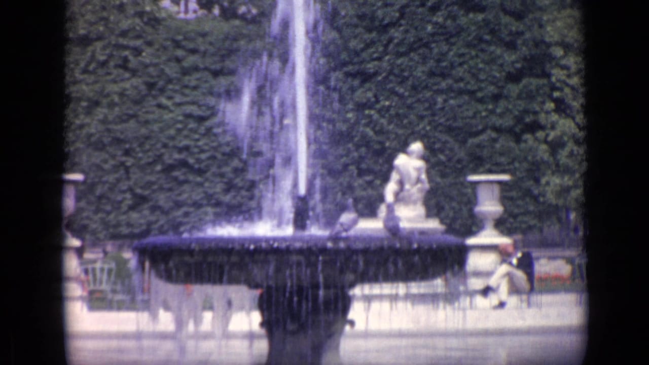 Fountain spraying beside a formal garden pond with statues and seated visitors nearby.