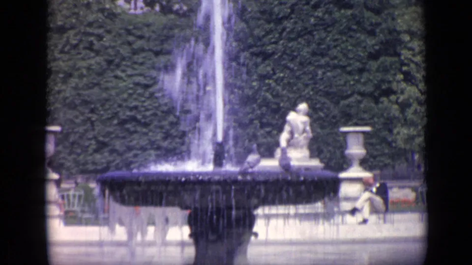 1962 8mm Versailles view of a fountain, stone basin, classical garden sculpture, and visitors beside the water.