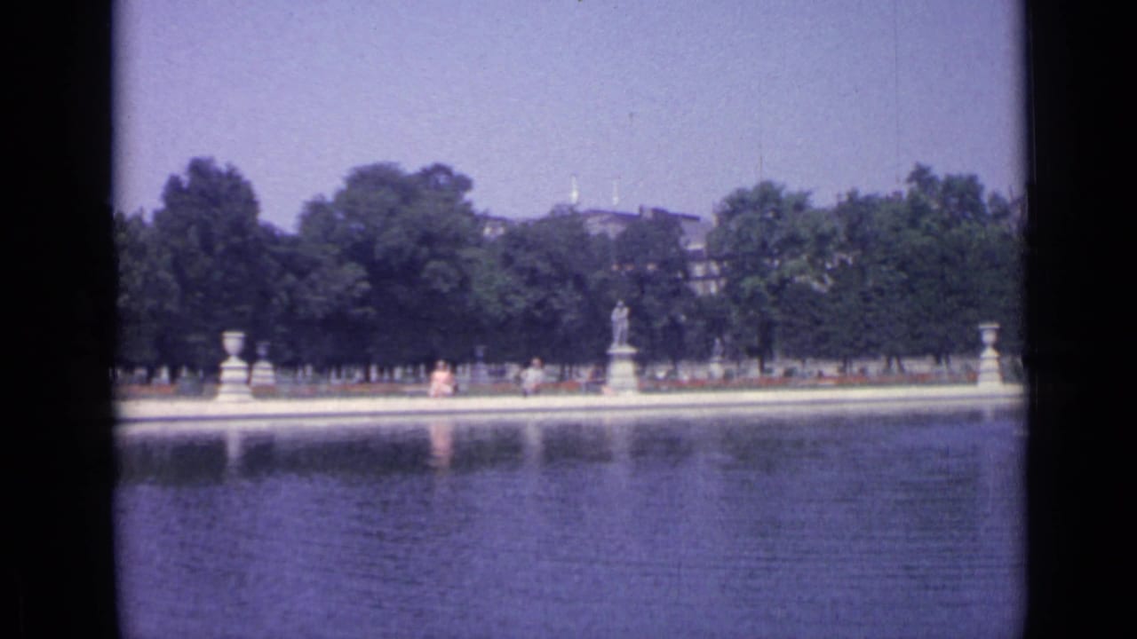 Wide 1962 Versailles garden view across the Grand Canal toward trees, stone figures, visitors, and distant architecture.