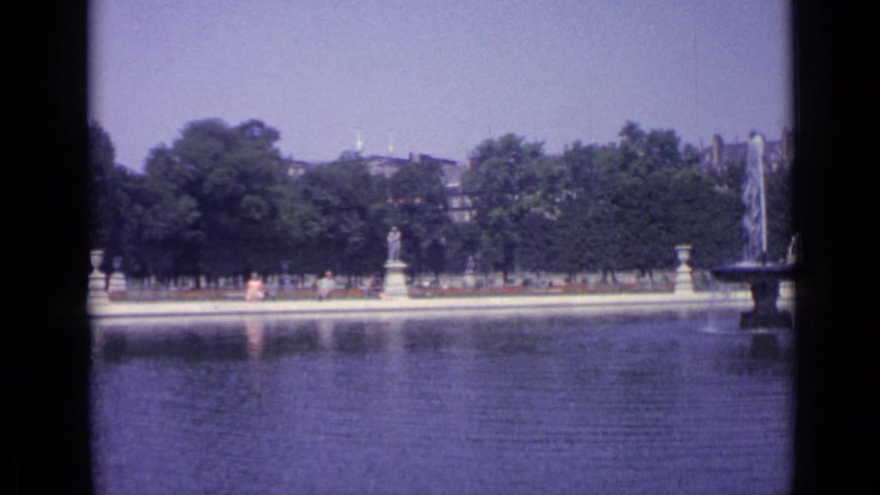 1962 Versailles canal scene with formal statuary, visitors along the far bank, trees, and a fountain partly entering frame.