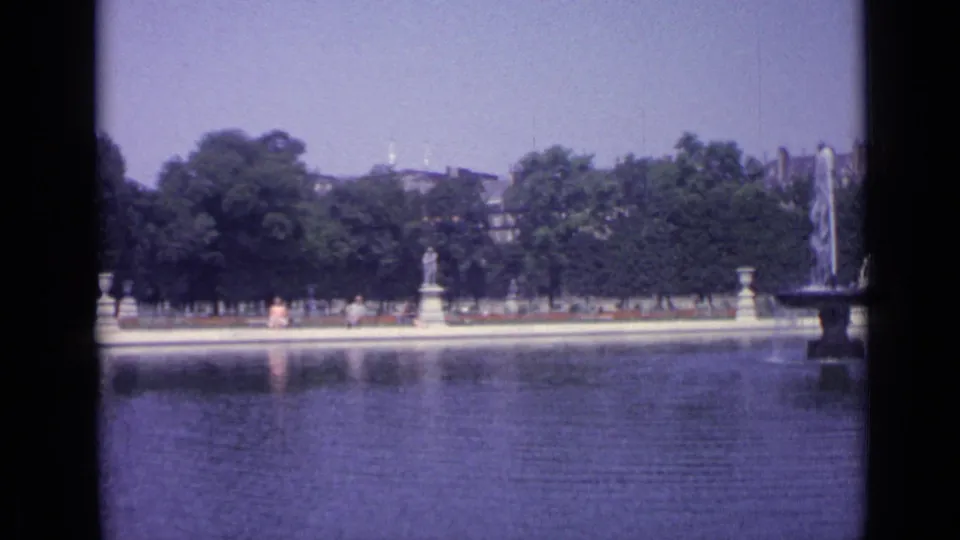 1962 Versailles canal scene with formal statuary, visitors along the far bank, trees, and a fountain partly entering frame.