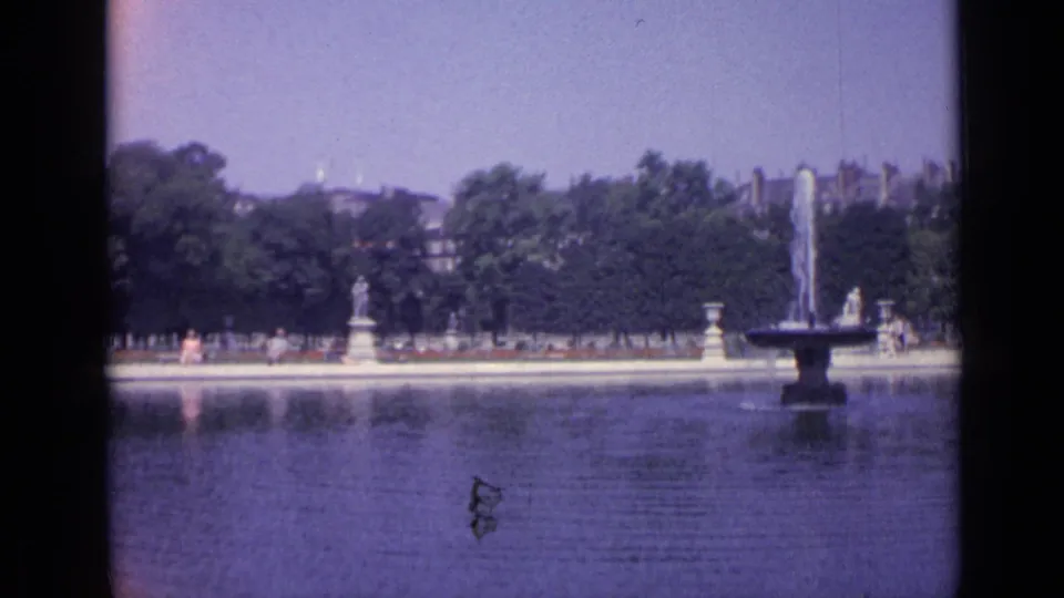Wide 1962 Versailles view of the Grand Canal, fountain spray, formal garden edge, trees, statues, and distant visitors.