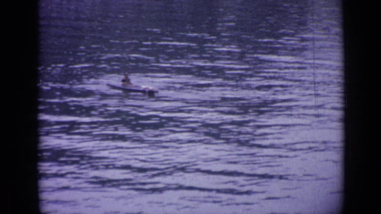 Wide home-movie view of a canoeist partly distant on the rippling lake water in Versailles.