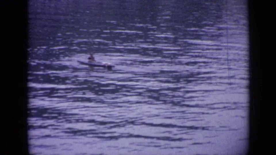 Wide home-movie view of a canoeist partly distant on the rippling lake water in Versailles.