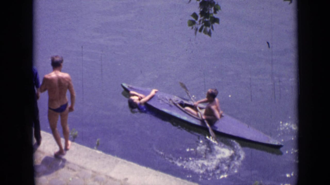 Canoe near a concrete shoreline in Versailles as a man in a blue swimsuit watches from the edge.