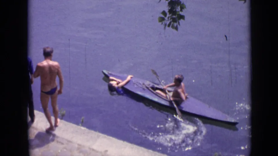 Canoe near a concrete shoreline in Versailles as a man in a blue swimsuit watches from the edge.