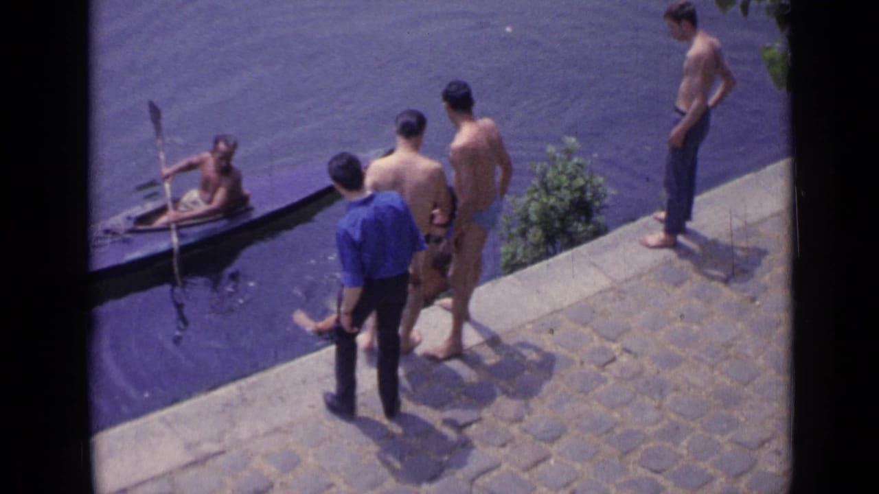 Men on a stone embankment beside dark water as a small boat approaches nearby.
