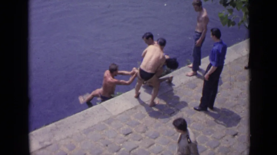 1962 Versailles home-movie frame showing several men pulling a swimmer toward the lakeside stone edge.