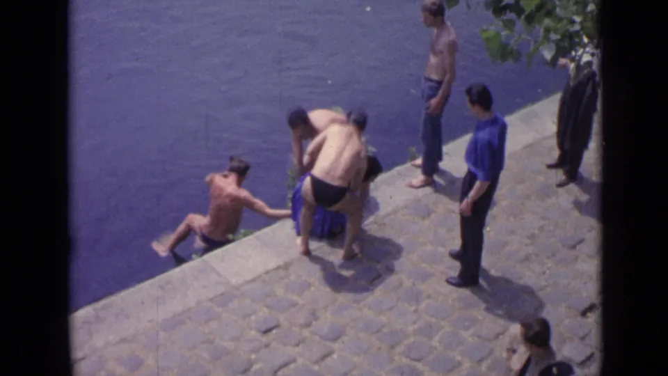 1962 Versailles frame with men clustered at the embankment, continuing to help a swimmer from the lake.