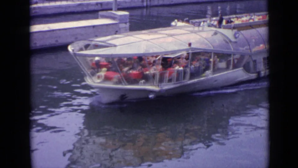 A glass-topped sightseeing boat carrying passengers cruises along the waterway in the 1962 Versailles home-movie footage.