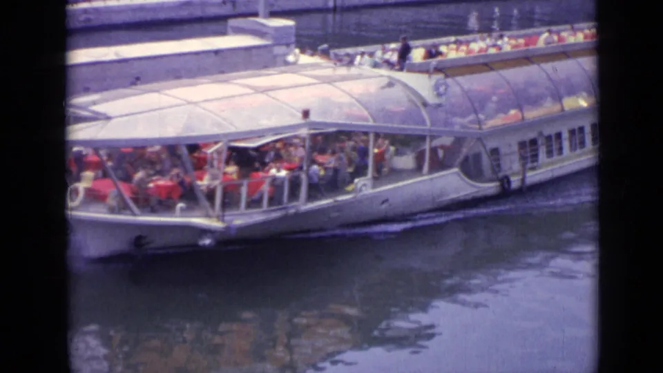 The 1962 Versailles clip ends on a glass-canopied passenger boat filled with tourists moving through the waterway.