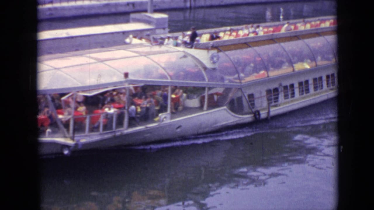 White tour boat with passengers moving along a canal beside a stone embankment.
