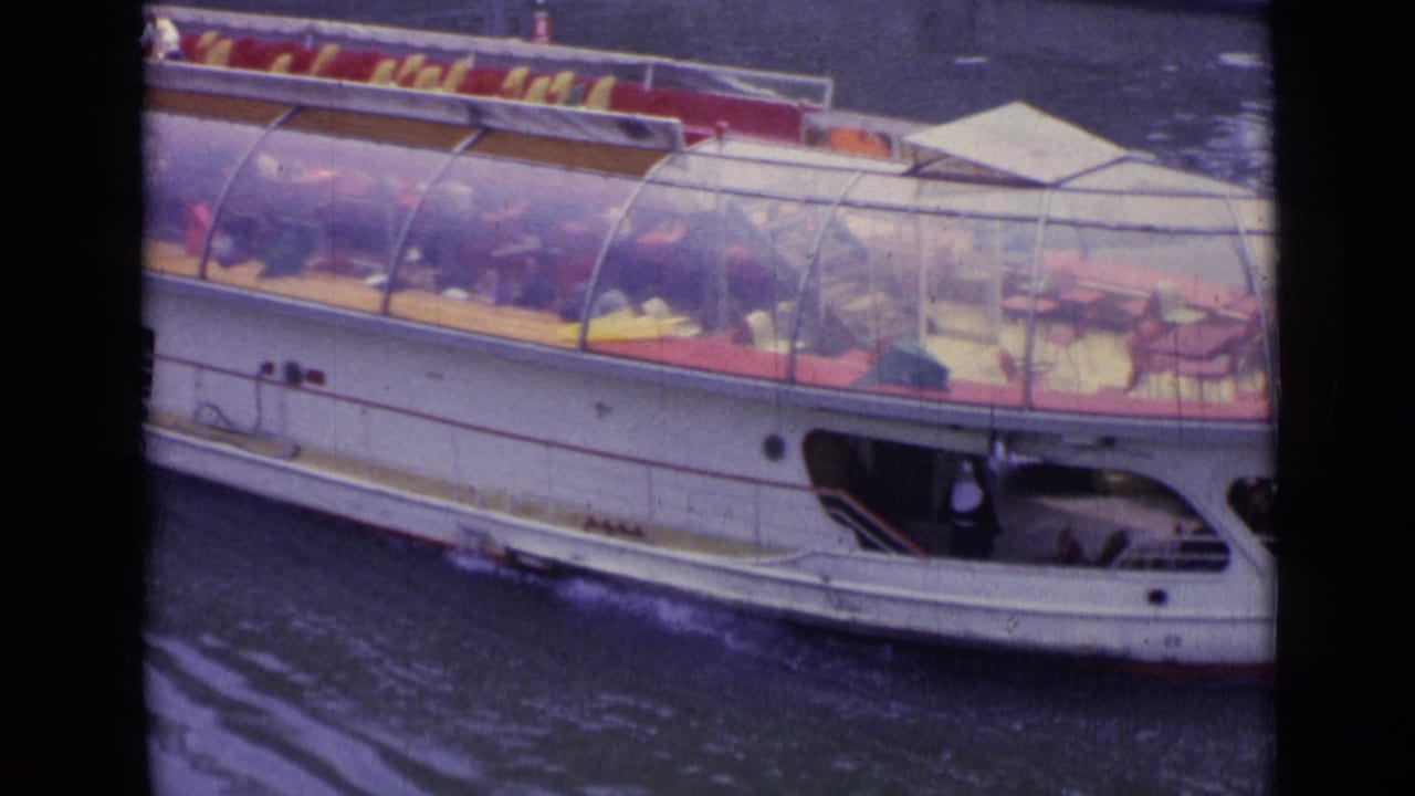 Large glass-domed passenger boat moving across a river with red seating visible inside.