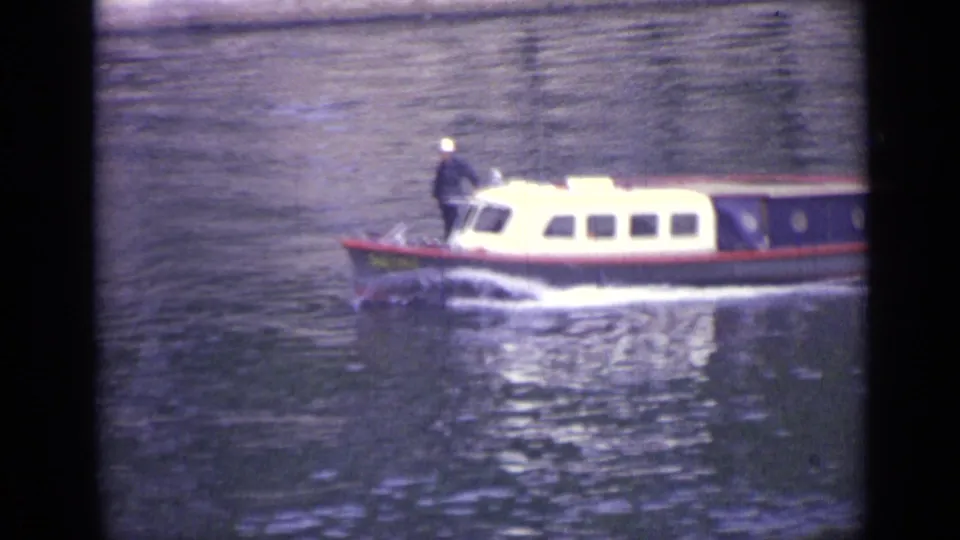 A larger white-cabin boat with a dark hull moves along the river, with a white-capped person standing near the front.