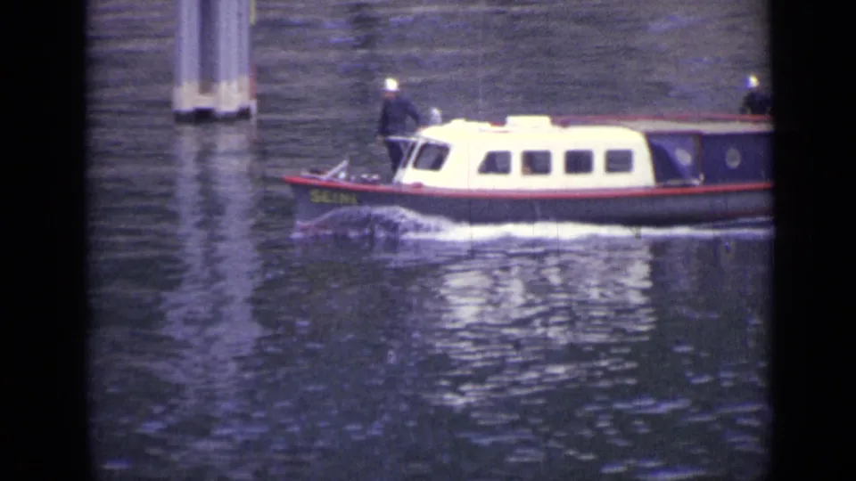 The white-cabin boat passes closer in the 1962 river scene, with side windows, dark hull, and possible lettering visible near the bow.
