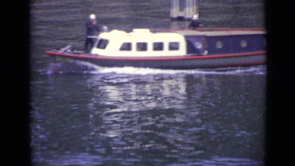 The cabin boat continues through the Versailles river footage, showing a standing white-capped operator, rectangular windows, and water reflections.