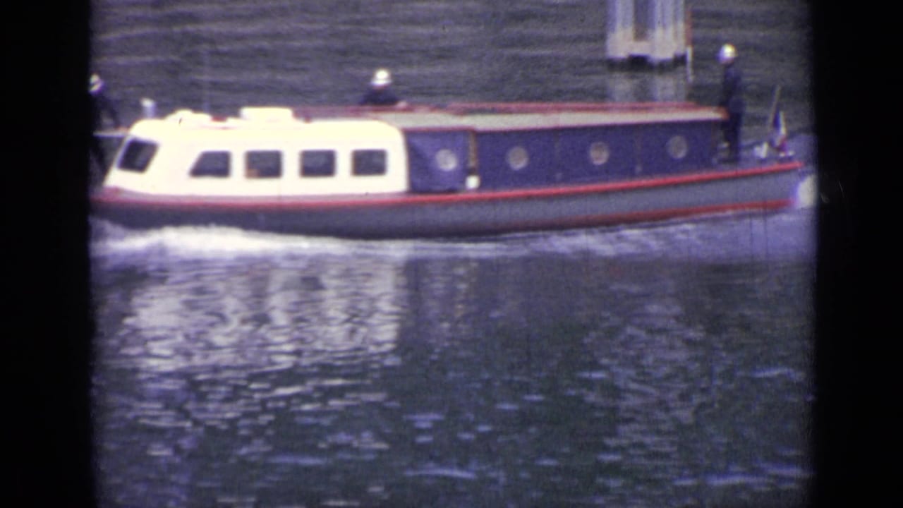 White and blue cabin boat moving across rippling water with dark vertical film borders.