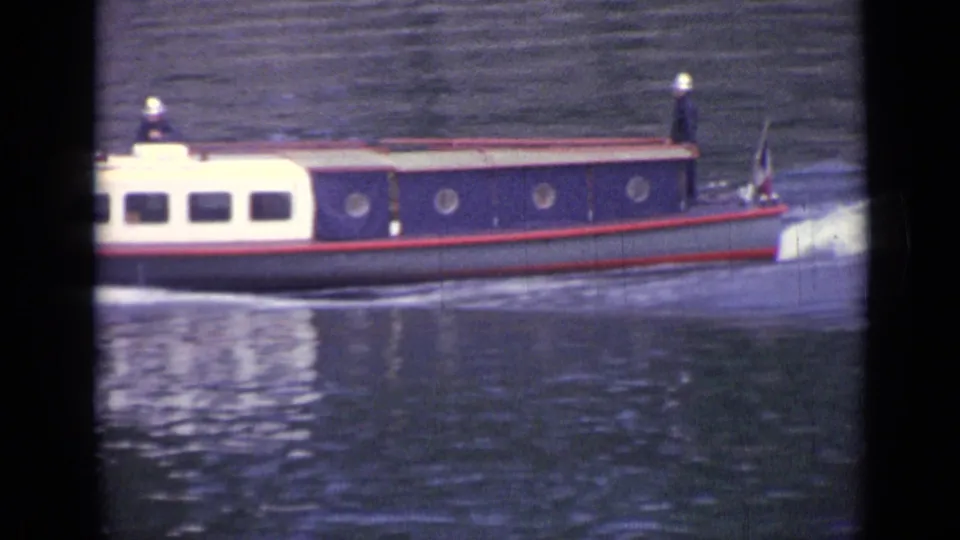 The blue and white boat continues along the Versailles waterway, leaving a bright wake behind it.