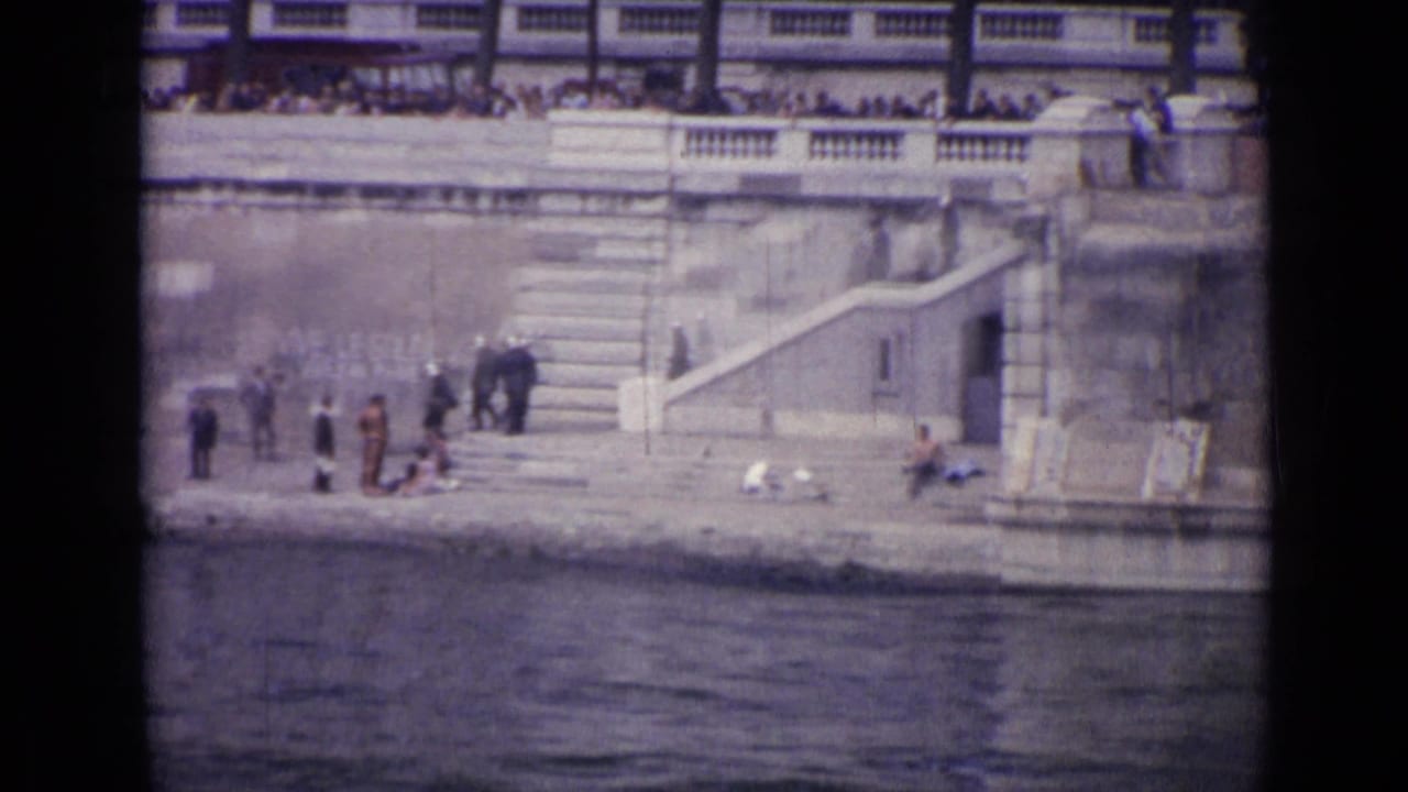 1962 Versailles home-movie frame showing people on a stone waterside embankment near stairs, with bystanders on the upper terrace.