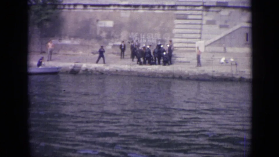 1962 Versailles frame with a cluster of uniformed men on the stone embankment, water in front and a stairway behind them.