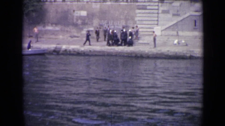1962 Versailles waterside frame showing uniformed men grouped on the embankment, with stairs, water, and distant onlookers visible.