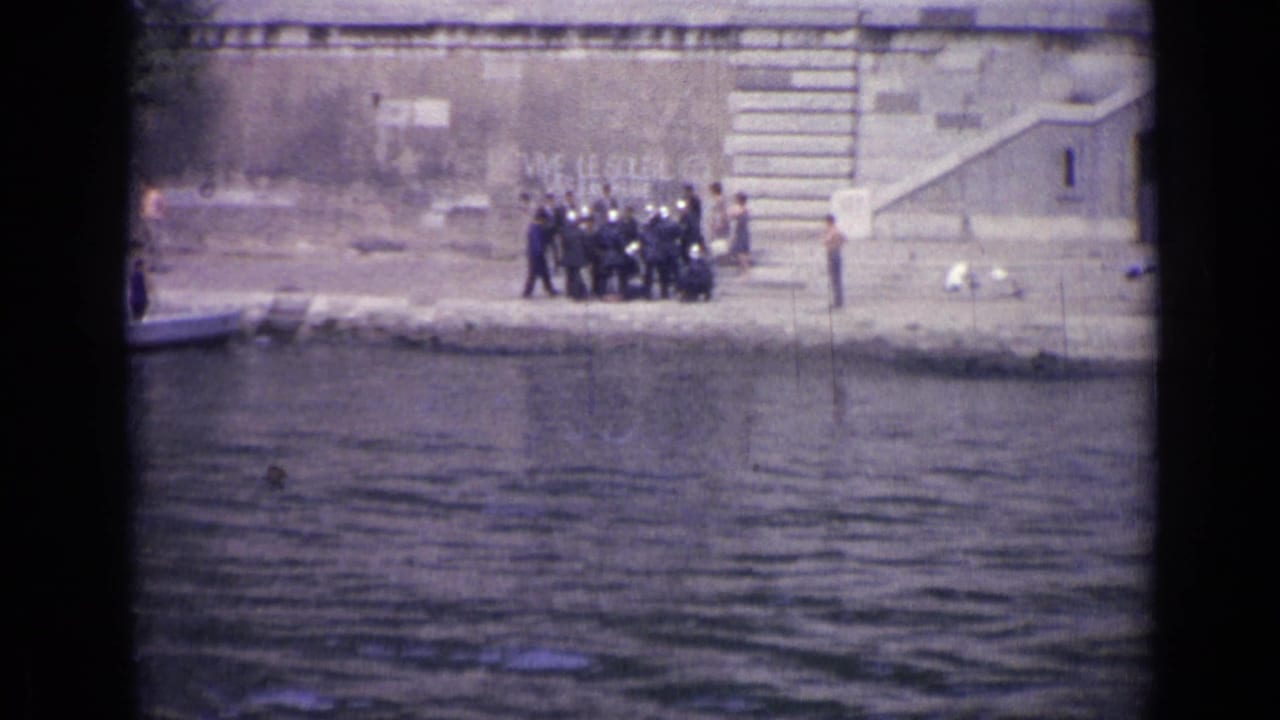 Group of people standing on a concrete riverbank beside water and a stone wall.