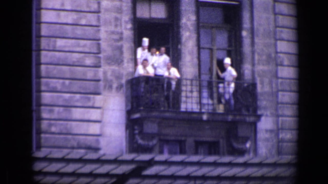 Chefs in white uniforms stand on a balcony of a stone building.