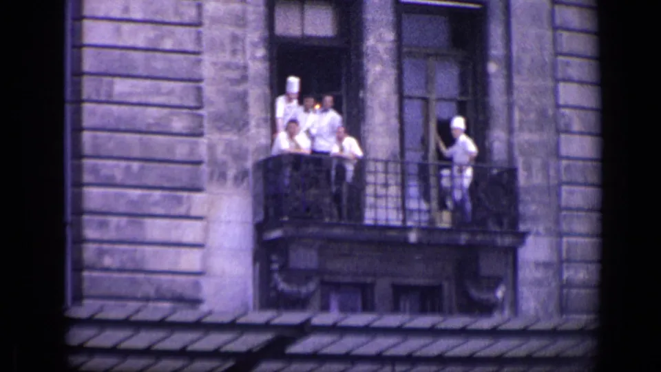 In 1962 Versailles, several chefs in white uniforms and toques stand on an iron balcony above the street.