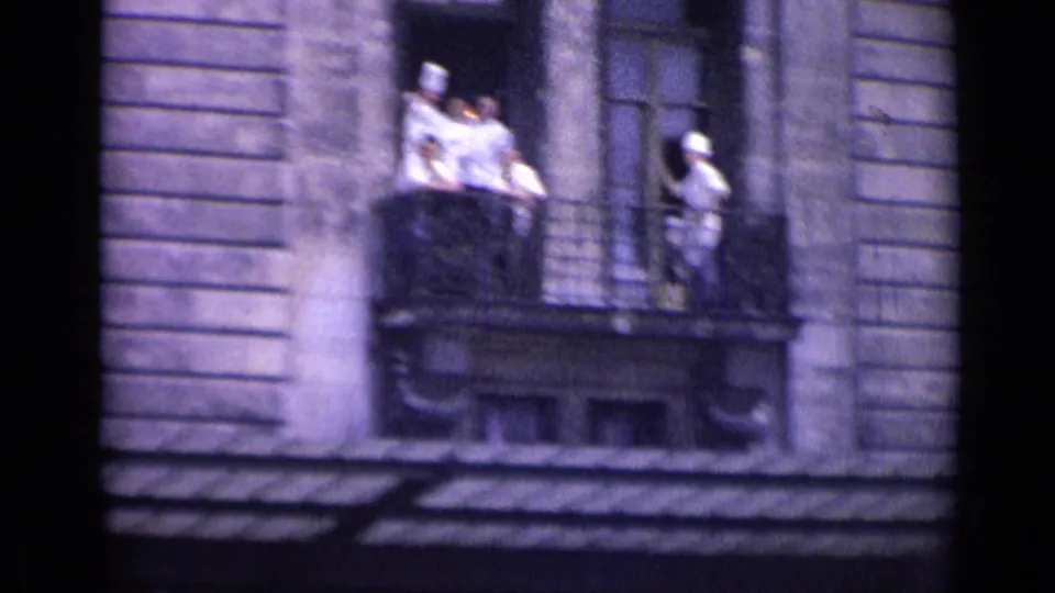 Chefs or kitchen staff in white uniforms appear on two balconies of a Versailles street building in 1962 footage.