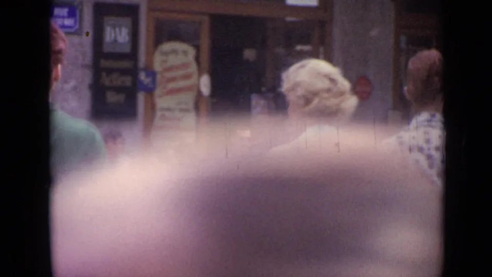A Versailles sidewalk scene shows pedestrians near a storefront with a DAB sign, partly obscured by close foreground blur.