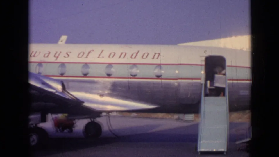 1962 airport frame showing a Skyways of London aircraft with its door open and a mobile stairway positioned beside the fuselage.