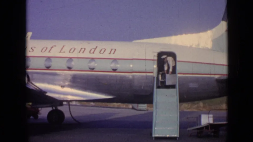 1962 home-movie frame showing a person at the top of mobile stairs beside a Skyways of London aircraft on the tarmac.