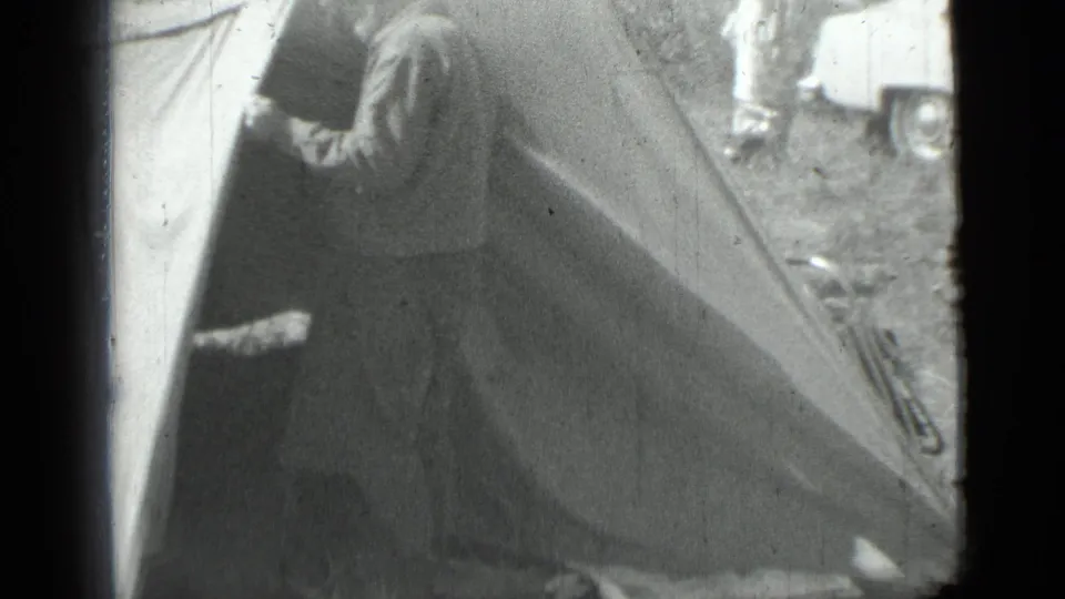 A closer 8mm frame shows the man at the canvas flap, with soft focus and background campsite details including a car and another person.
