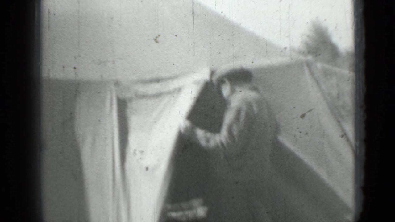 Black-and-white home-movie frame from the supplied 1967 clip showing a woman standing or walking beside a large tent in a field.