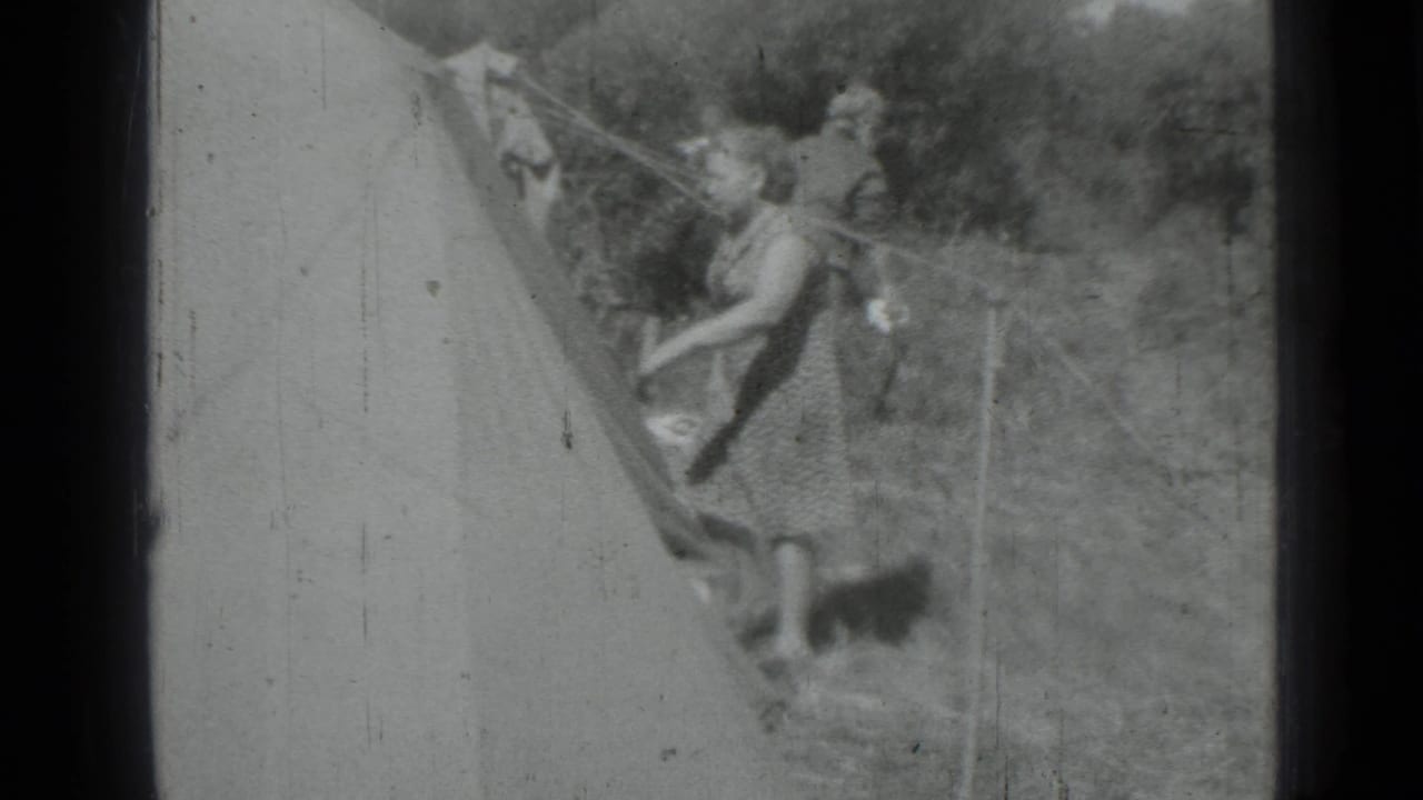 Two women work beside a sloped canvas tent in a grassy campsite.