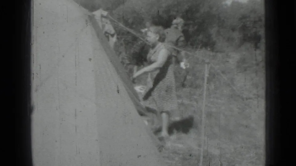 1967 8mm home-movie frame from Saint Petersburg metadata showing two women adjusting a tent at a wooded campsite.