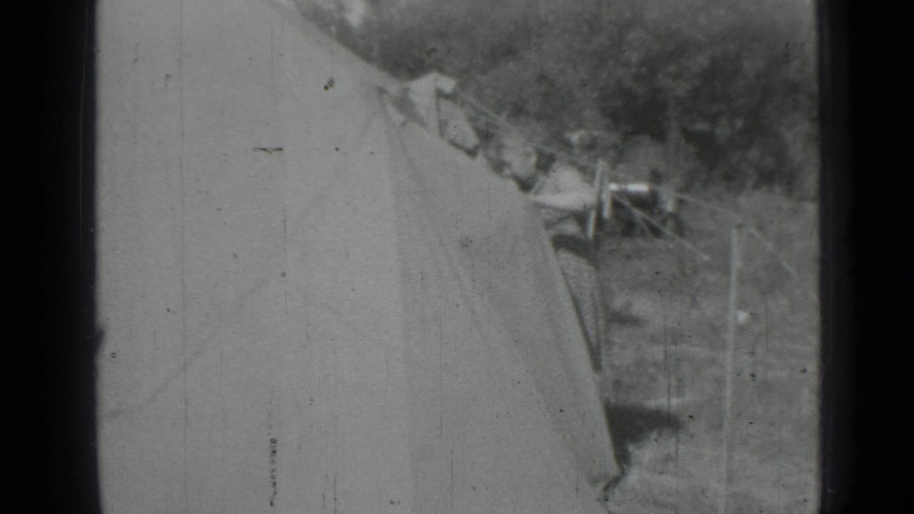 Canvas tent beside a grassy clothesline area with a person partly visible near hanging fabric.