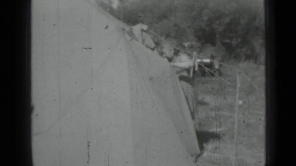 1967 home-movie frame from Saint Petersburg metadata showing a canvas tent, grass, trees, clothesline poles, and a partly visible adult near fabric.