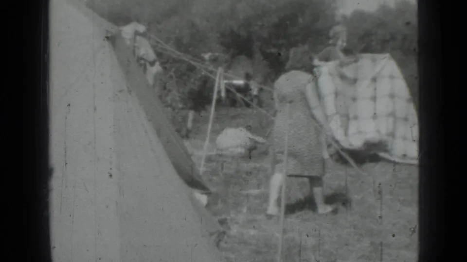 Two adult women appear beside sheets or towels on a clothesline near a canvas tent in the Saint Petersburg 1967 home-movie setting.