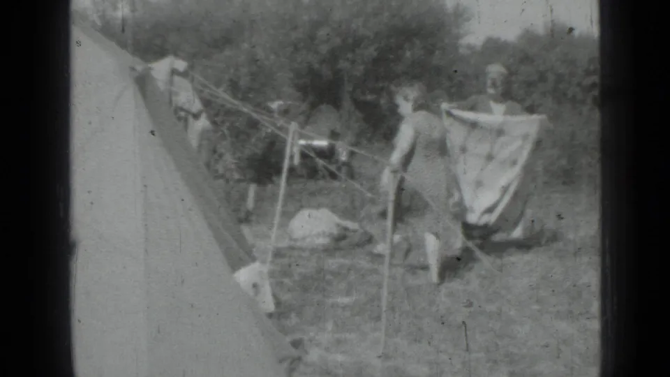 Adult women handle a large hanging sheet or towel beside clotheslines and a canvas tent in the Saint Petersburg 1967 home-movie footage.