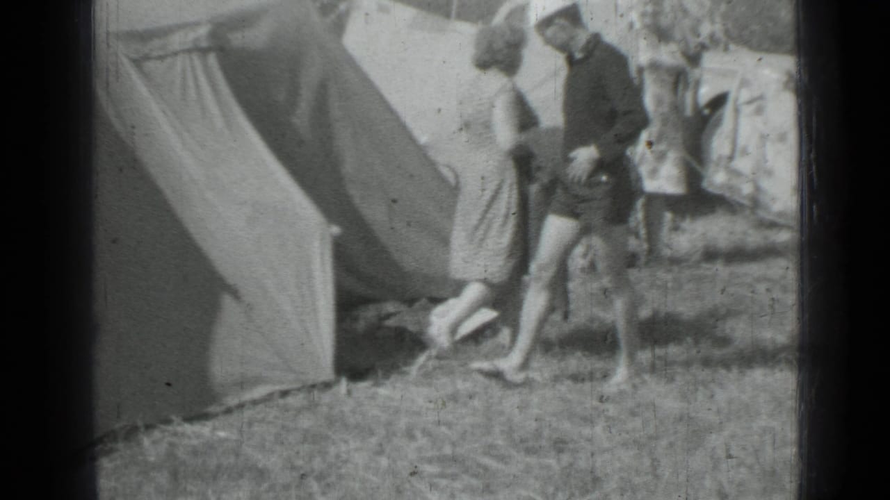 Adults walking beside a canvas tent at a grassy campsite.