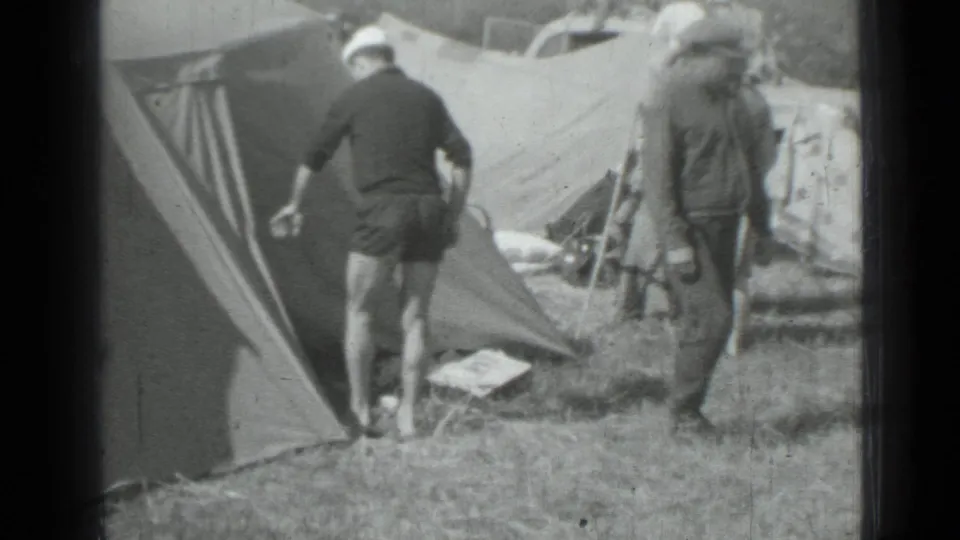 1967 home-movie frame from Saint Petersburg showing adults near canvas tents at a grassy campsite.