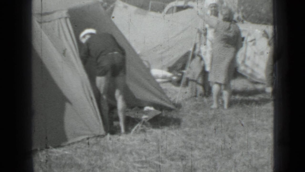 1967 campsite frame showing a man leaning into a canvas tent while a woman stands beside camping gear.