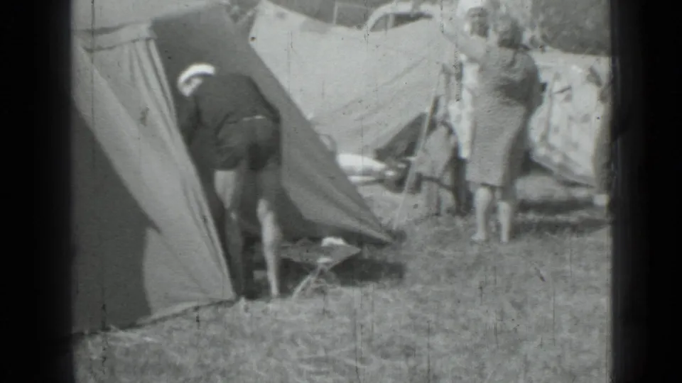 1967 campsite frame showing a man leaning into a canvas tent while a woman stands beside camping gear.