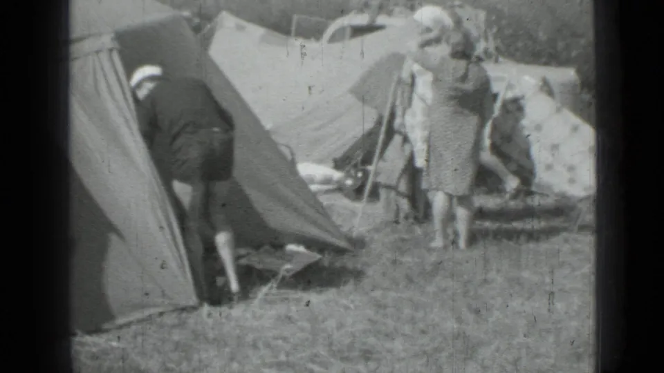 Black-and-white 8mm frame of adults around canvas tents and campsite gear in Saint Petersburg, 1967.